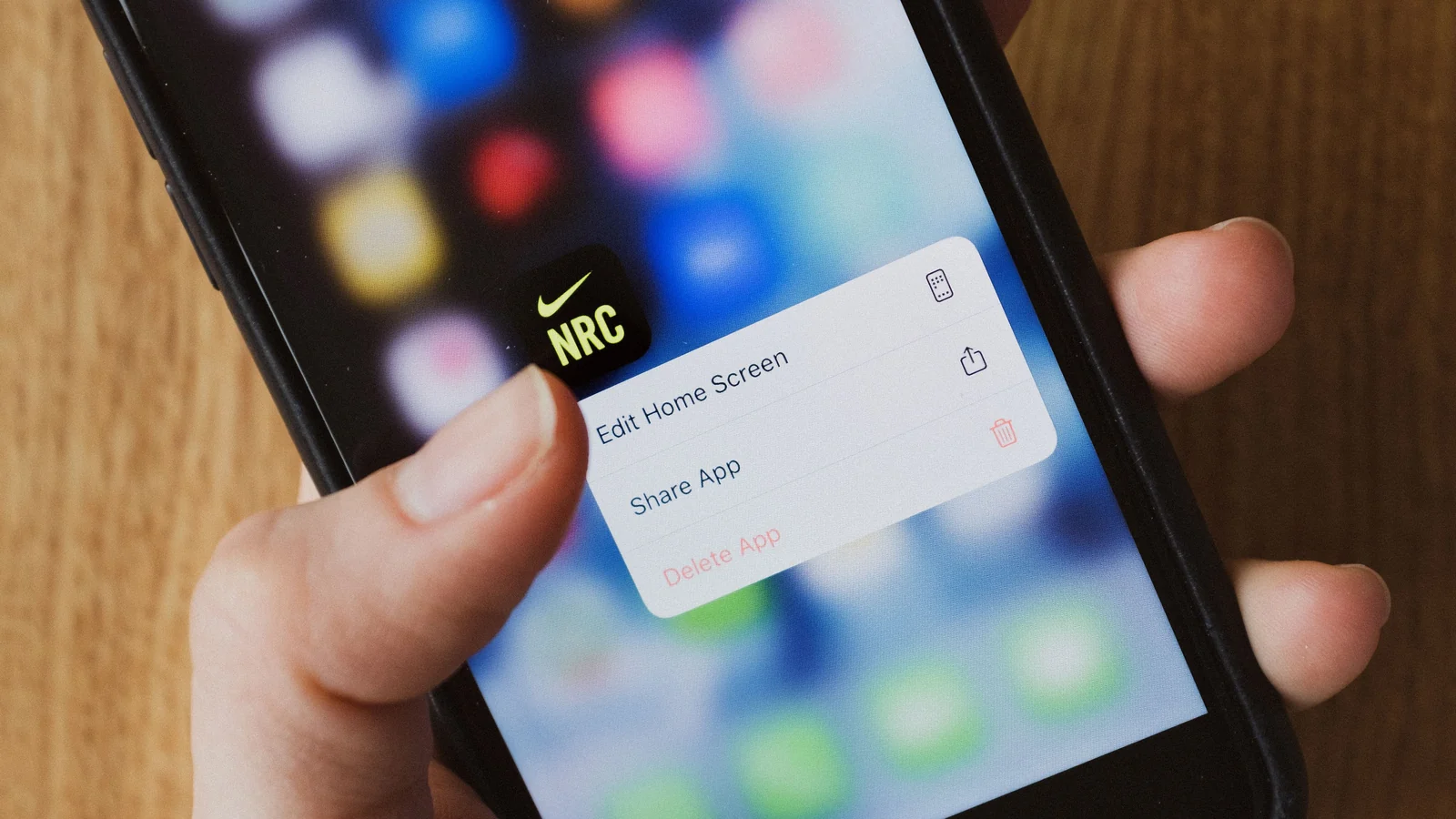 A hand using a smartphone on a wooden desk with a sharing menu visible on the screen