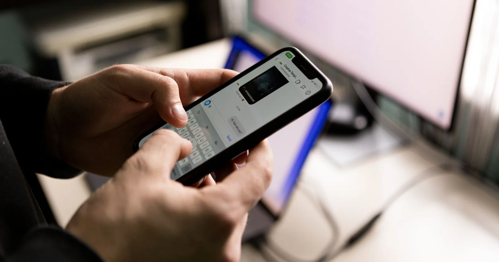Person holding a smartphone beside a computer while using a chat app