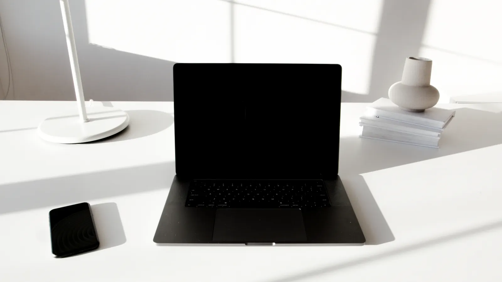 A black laptop and smartphone on a bright white desk prepared for sending an email attachment