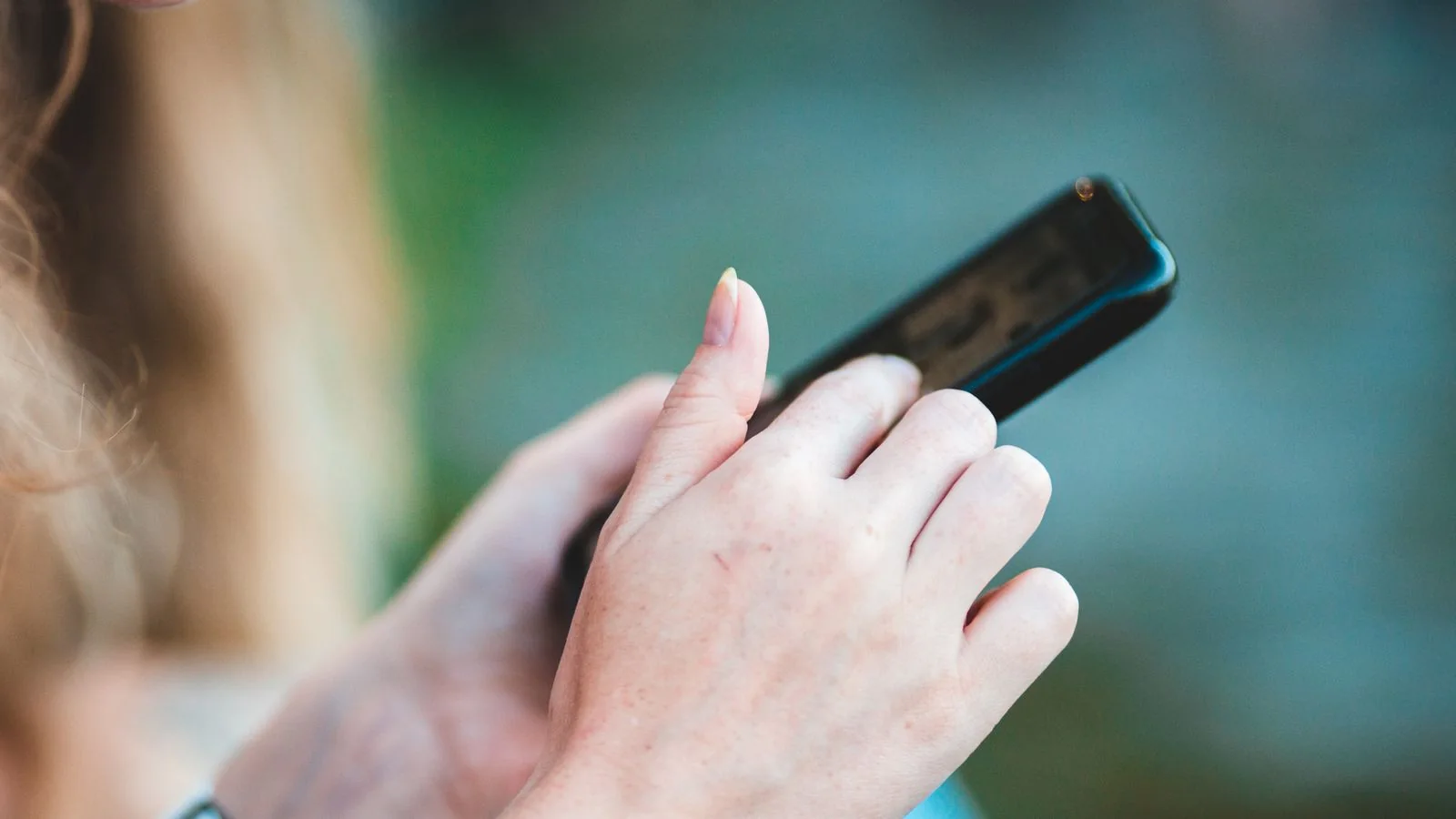 Close-up of a person using a smartphone with the screen turned away against a soft blue background