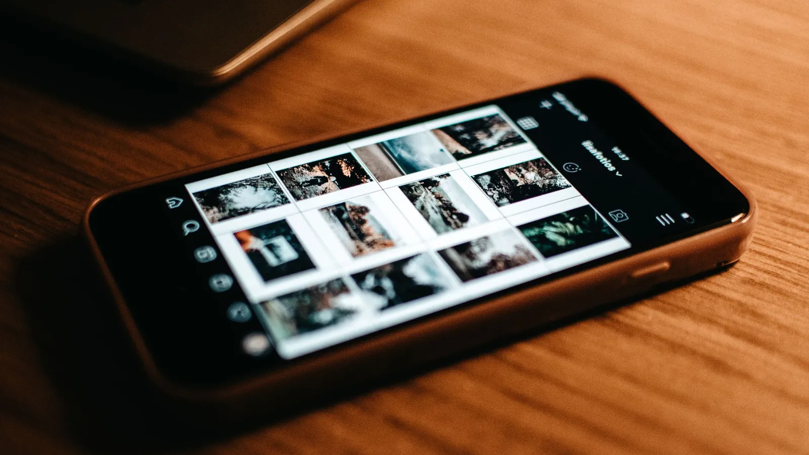 A smartphone displaying a photo gallery beside printed pictures on a wooden desk