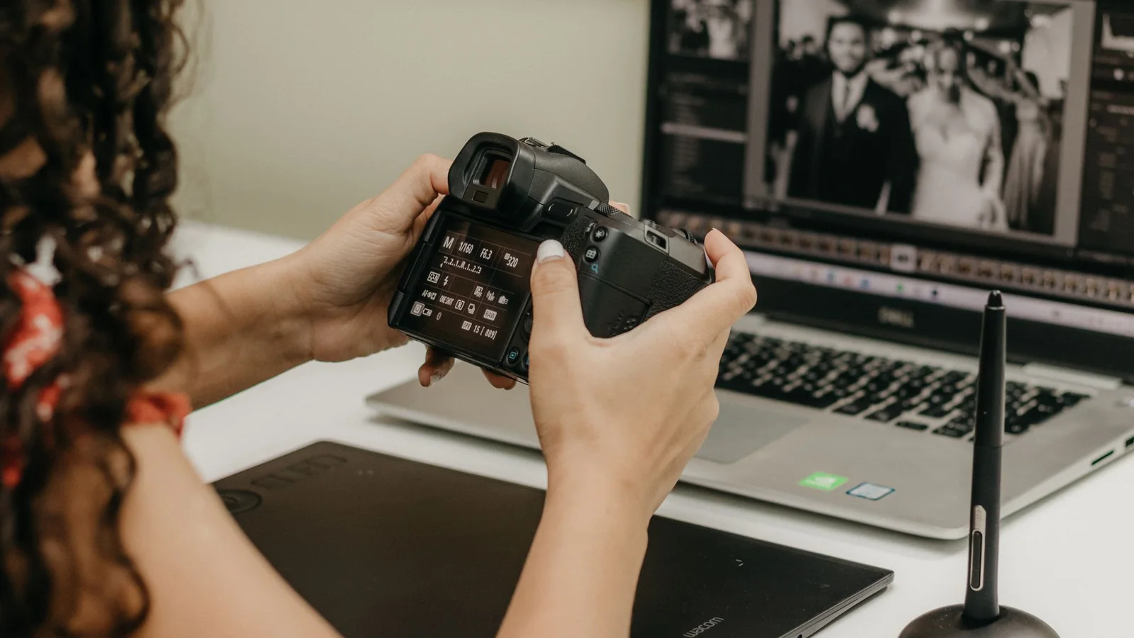 A photographer holding a camera while reviewing photos and metadata on a laptop