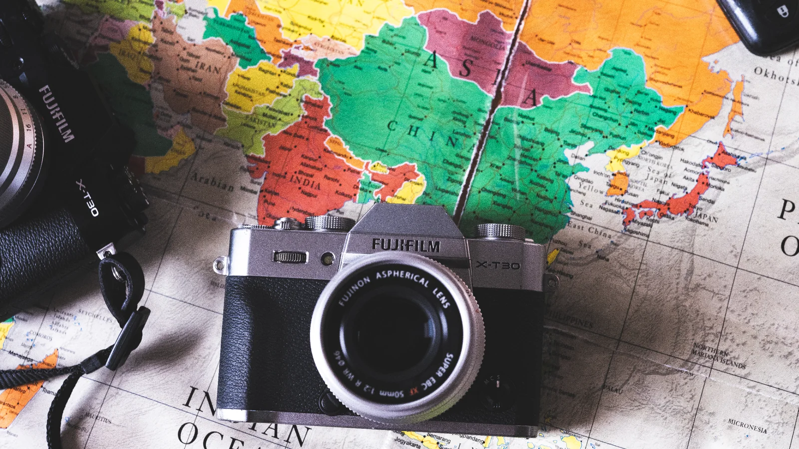 A camera resting on a colorful world map to illustrate finding a photo location from embedded GPS metadata