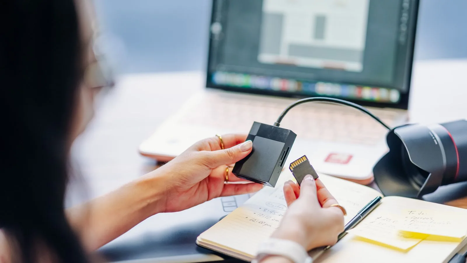A photographer holding an SD card beside a camera and laptop before inspecting photo EXIF data