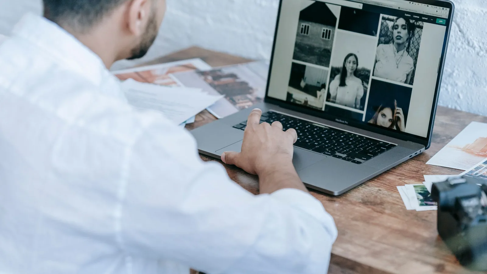 A photographer using a laptop beside printed photos and a camera while reviewing XMP metadata